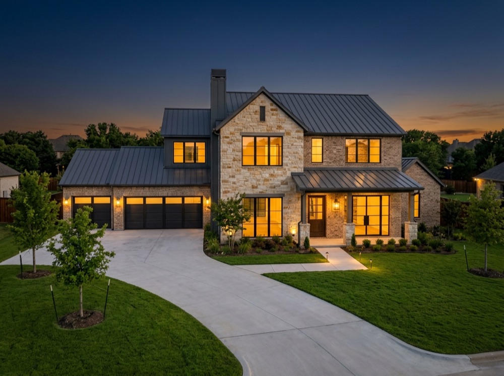 A newly completed stone-and-brick custom home at dusk, windows lit from inside.